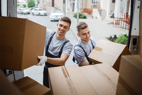Two-young-handsome-smiling-movers-wearing-uniforms-are-unloading